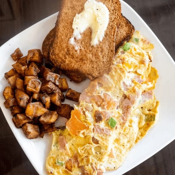 A breakfast plate with a fluffy omelet, crispy home fries, and buttered toast.