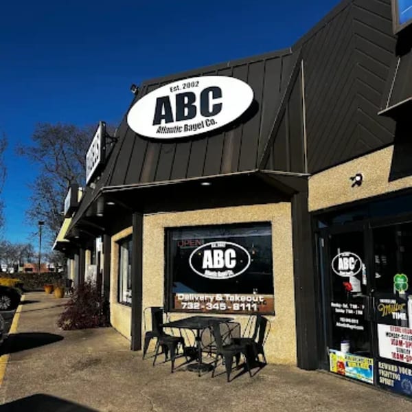 Exterior of Atlantic Bagel Co. with a black roof, tan walls, and outdoor seating under a clear sky.
