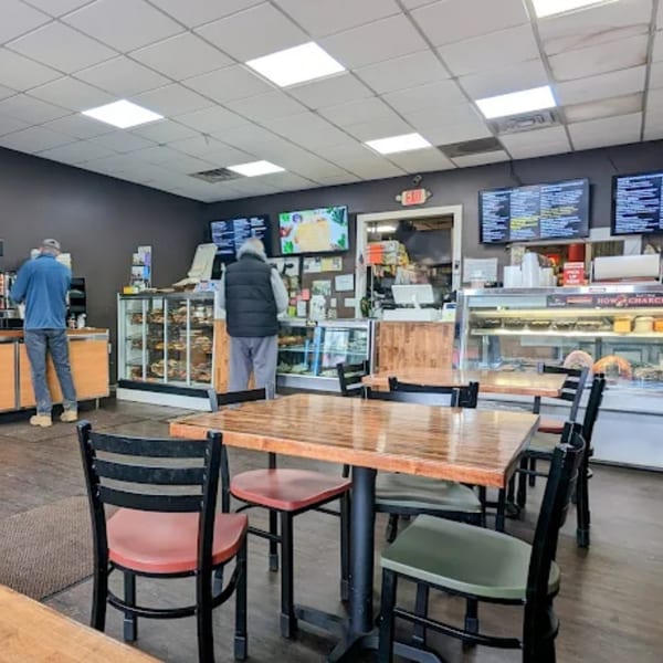 Interior of Atlantic Bagel Co. with customers at the counter, display cases, and empty dining tables.