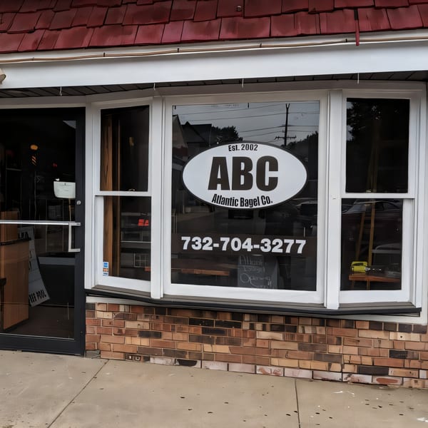 Exterior of Atlantic Bagel Co. storefront with a large window displaying the "ABC Atlantic Bagel Co." logo and phone number.