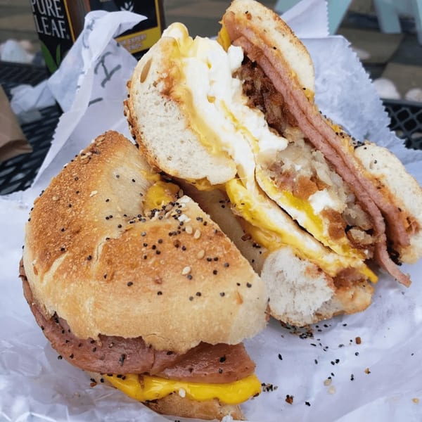 An Atlantic Bagel Co. everything bagel, cut in half, filled with egg, cheese, hash brown, and meat.