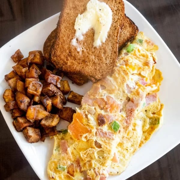 A breakfast plate with a fluffy omelet, crispy home fries, and buttered toast.