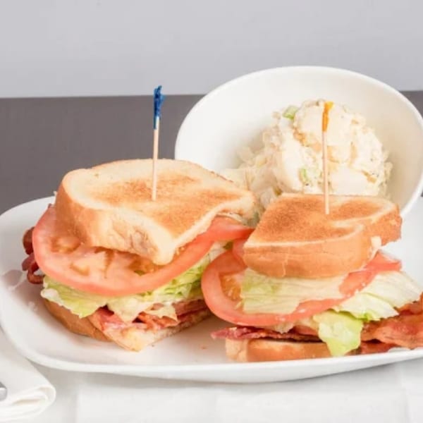 Two toasted sandwiches with bacon, lettuce, and tomato, served with a side of potato salad.