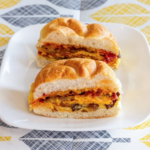 Two halves of a bagel sandwich filled with egg, cheese, and bacon on a white plate.