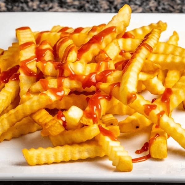 A close-up of golden crinkle-cut fries generously drizzled with bright red ketchup on a white plate.