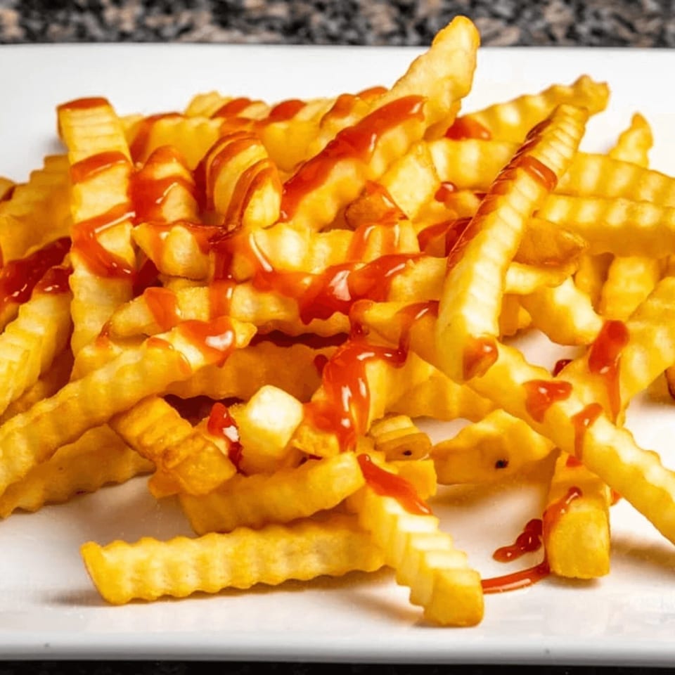 A close-up of golden crinkle-cut fries generously drizzled with bright red ketchup on a white plate.