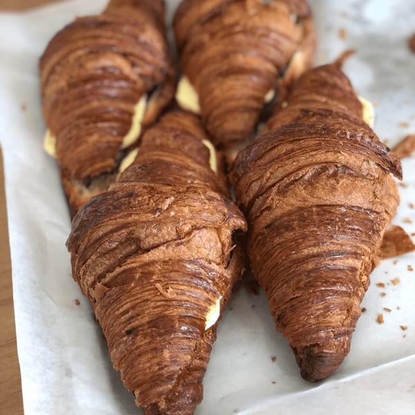 Several golden-brown croissants with creamy filling, arranged on white parchment paper.