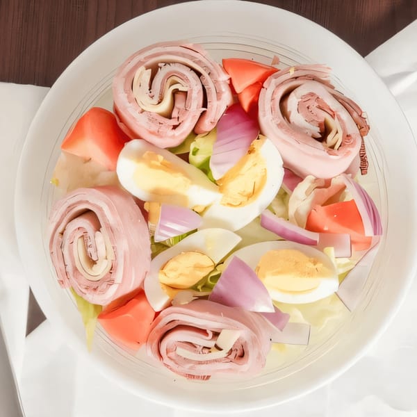 Overhead view of a chef salad with rolled deli meat, hard-boiled eggs, tomatoes, and red onion.