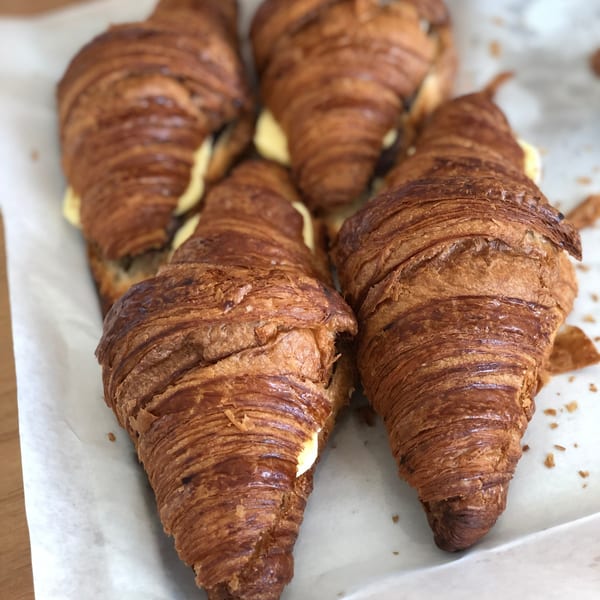 Close-up of several golden-brown croissants with creamy filling, on white parchment paper.