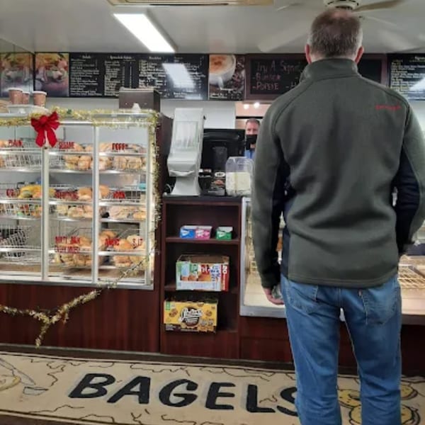 Customer facing the counter at Atlantic Bagel Co., with a display case full of bagels.