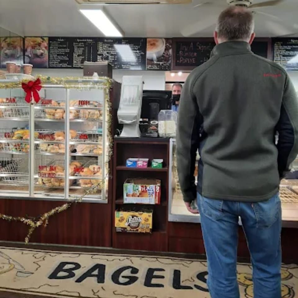 Customer facing the counter at Atlantic Bagel Co., with a display case full of bagels.