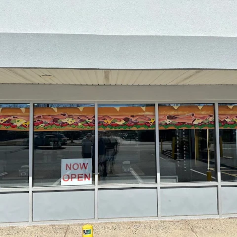 Exterior of Atlantic Bagel Co. with a "NOW OPEN" sign and a mural of a large sandwich.