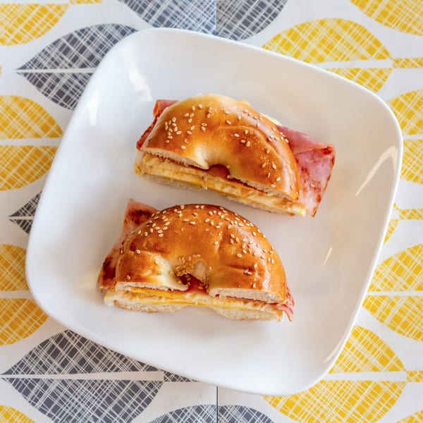 Two Atlantic Bagel Co. breakfast sandwiches with ham, egg, and cheese on sesame bagels.